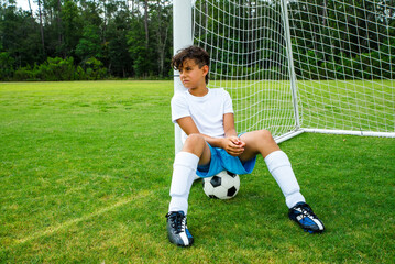 Tired young male soccer player sitting on a soccer ball in the goal, looking exhausted after a...