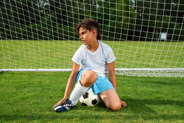 Tired young male soccer player sitting on a soccer ball in the goal, looking exhausted after a game