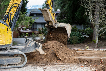 Excavator with large bucket picking up dirt from the road and piling it up, road construction project
