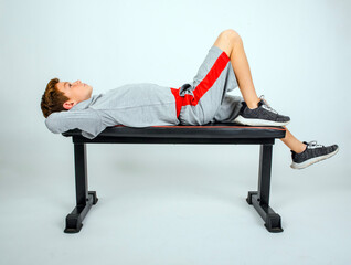 Obraz premium Young preteen male athlete in a grey sweatshirt and shorts, lying back on a bench, hands behind head, looking up and thinking about the game