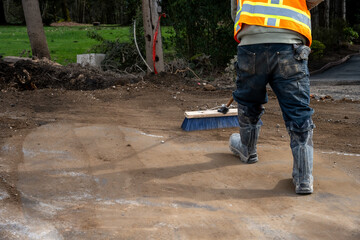 Construction worker with push broom cleaning dirt off road from stump removal during a road...