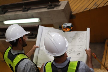Two skilled electric train engineers are diligently surveying and checking to ensure the plan matches the blueprint and survey camera in the electric train maintenance shop, to submit work on the spec