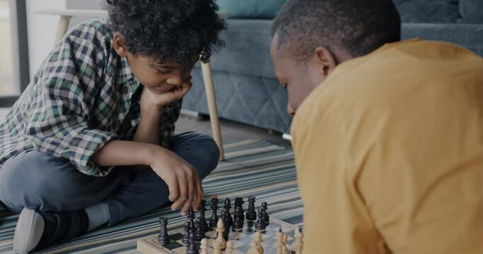 Smart little boy playing chess with caring father African American man moving pieces on board enjoying game at home. Childhood and family concept.