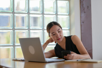 Businesswoman Reviewing Information on Smartphone and Laptop