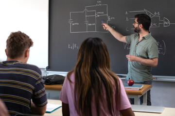 Male caucasian teacher pointing blackboard explaining new concepts to multiracial high school...