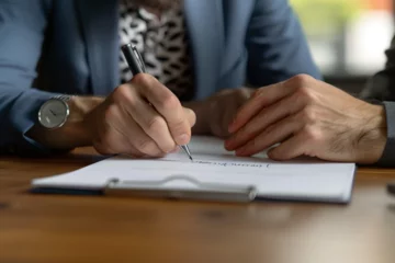 Fotobehang Focused young businessman signing agreement with skilled lawyer in eyeglasses. Concentrated financial advisor showing place for signature on paper contract document to male client at meeting in office © Zoraiz
