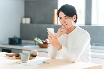 ダイニングで朝食を取りながらスマホを見る若いアジア人男性
