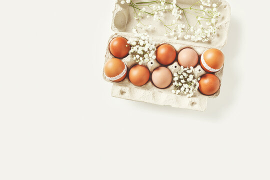 Easter eggs decorated lace and white spring flowers in carton box on light background. Easter holiday, aesthetic top view of festive chicken egg in container, springtime life still, vintage toned