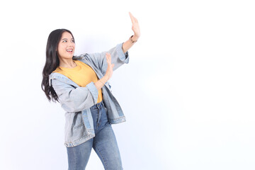 Beautiful Asian woman in blue jacket yellow t-shirt makes stop gesture, demonstrates rejection...