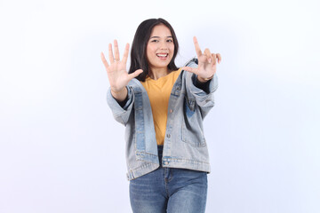 Young beautiful Asian woman wearing blue jacket yellow t-shirt showing number 7 and pointing up...