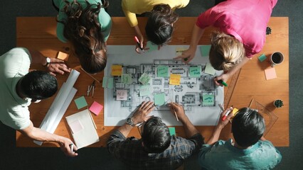 Top down of skilled business people holding tablet an looking at blueprint. Aerial view of architect engineer planning and design house design together while standing at table with laptop. Symposium. - obrazy, fototapety, plakaty