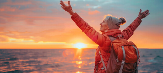 Confident mature woman with backpack with arms up relaxing at sunset seaside during a trip , old...
