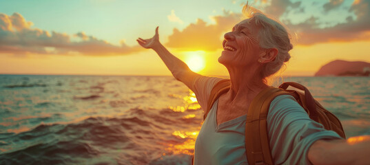 Confident mature woman with backpack with arms up relaxing at sunset seaside during a trip , old female traveler enjoying freedom in serene nature landscape