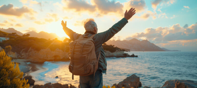 Confident mature man with backpack with arms up relaxing at sunset seaside during a trip , old male traveler enjoying freedom in serene nature landscape