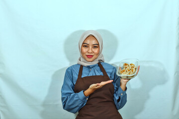 beautiful Asian woman in a brown apron and hijab holding a bowl of dim sum or dumplings isolated...