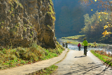 The woman is riding a bicycle along Dunajec river in autumn sunny day, Pieniny mountains located near  Szczawnica