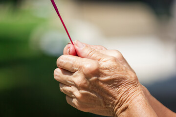 Action of old woman hand is holding incense stick  for praying to the ancestors at the cemetery to...