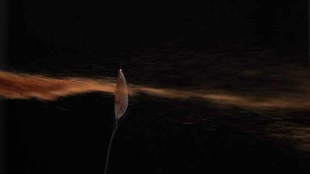 Slow motion of sprinkling cocoa from a small spoon in dark studio