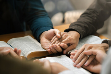 Obraz na płótnie Canvas Group of young Christians praying, holding hands and praying together The concept of praying to God in the home as a team Pray to God with the Bible for forgiveness and faith.