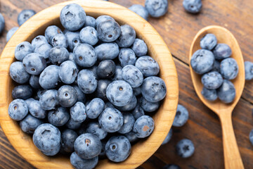 Ripe blueberries in a wooden bowl and spoon on a background of scattered berries. Concept of healthy and dieting eating.
