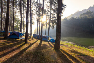 Group of tent for overnight camping with sunrise over misty mountain and ray of light and campsite...