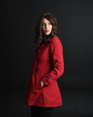 close up portrait of beautiful brunette woman model, wearing red trench coat.isolated on dark studio background with shadows.  hands in jacket pockets.