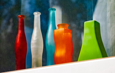 Multicolored glass decorative bottles on a white window sill against a background of greenery