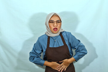 young housewife woman in hijab, glasses and brown apron, Having abdominal pain, put hands on stomach on white background. People housewife muslim lifestyle concept
