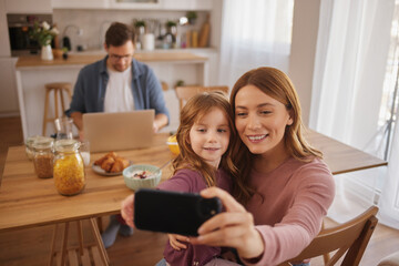 Mother and daughter taking Selfie with smart phone during breakfast at home