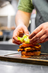 A skilled chef meticulously assembles a gourmet burger, showcasing vibrant, fresh ingredients and culinary artistry
