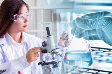 Attractive scientist woman testing chemical sample in flask at laboratory with lab glassware background. Science or chemistry research and development concept	