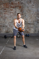 Full-length portrait of a focused shirtless young man playing basketball on a gray background in a gym