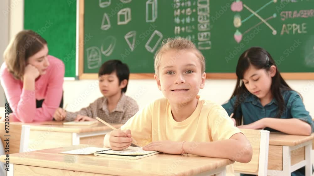 Aufkleber caucasian smart child smiling at camera while doing classwork at classroom while happy multicultural
