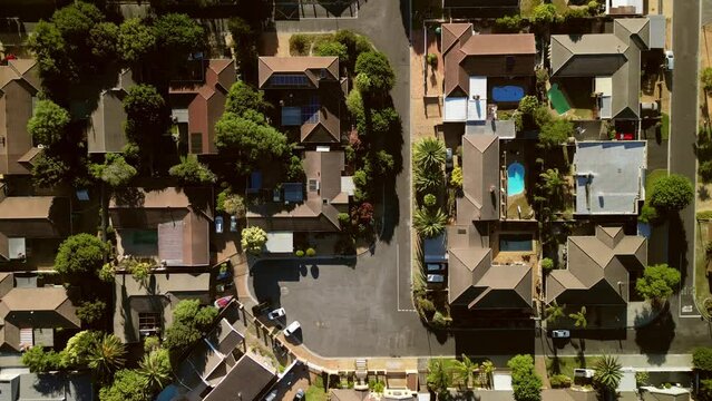 An aerial perspective reveals the layout of a suburban neighborhood during the golden hours of sunset. The roofs of houses, backyard swimming pools, and well-manicured gardens create a patterned mosai