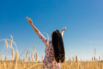 A woman, a girl stands backwards in a wheat field with her hands raised to the sky.