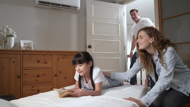 Bedtime story with childhood storytelling, mom and dad reading a fantasy book together to their little young girl in cozy and comfortable bedroom. Modern family happy time. Fastidious