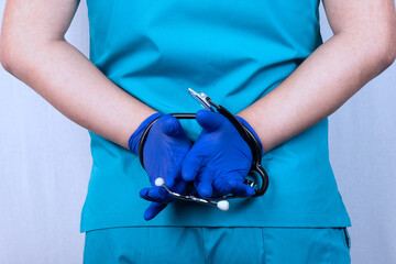 A doctor in blue uniform with a stethoscope tied in his hands. The concept of obligations, restrictions, contracts, crimes. - obrazy, fototapety, plakaty