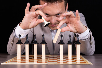 A businessman is building a pyramid of chess pieces and wooden blocks. The concept of construction,...