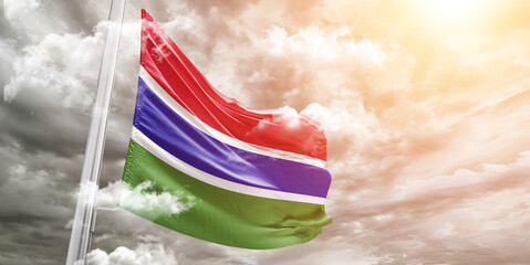 The Gambia national flag cloth fabric waving on beautiful cloudy Background.