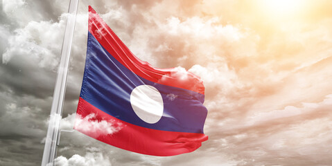 Laos national flag cloth fabric waving on beautiful cloudy Background.