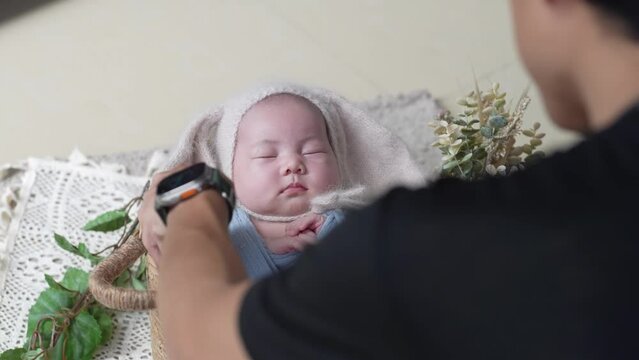 A Japanese photographer in his 30s taking a newborn photo of a 32-day-on Taiwanese baby wrapped in a blue wrap 30代の日本人カメラマンが青いおくるみを巻かれた生後32日の台湾人の赤ちゃんのニューボーンフォトを撮影する様子