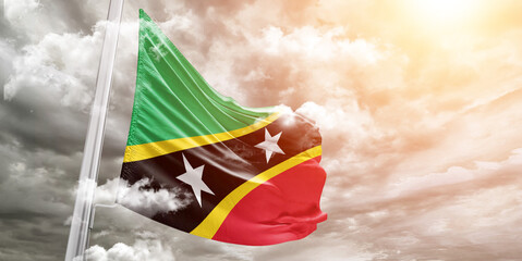 Saint Kitts and Nevis national flag cloth fabric waving on beautiful cloudy Background.