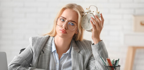 Young thoughtful businesswoman with alarm clock trying to meet deadline in office. Time management...