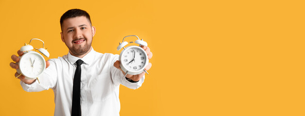 Young happy businessman with alarm clocks on yellow background. Time management concept