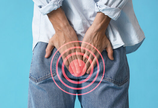 Young man with hemorrhoids on blue background, back view