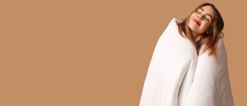 Beautiful young happy woman with soft blanket on brown background