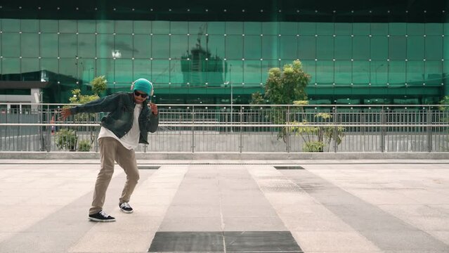 Happy hipster listen to hip hop music from headphone while dancing in lively mood. Professional street dancer perform b boy dancing at outdoor. Outdoor sport 2024. Modern lifestyle. Sprightly.