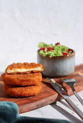 Fresh made and cutted fried camembert cheese with a side of fresh salad on wooden plate, white marble table