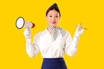 Beautiful Asian stewardess with megaphone on yellow background