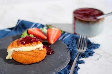 Fresh made fried camembert cheese with cranberry sauce on top, grey stone plate
